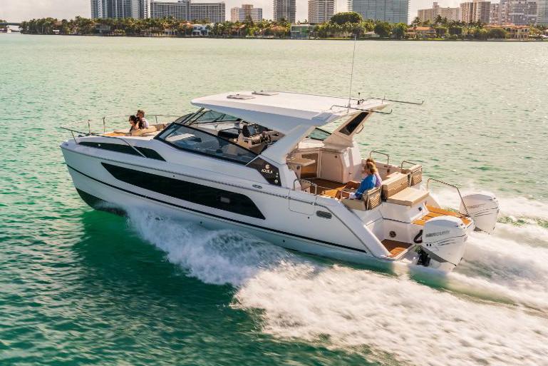 Luxury motorboat cruising through turquoise waters, with two people onboard and city skyline in the background.